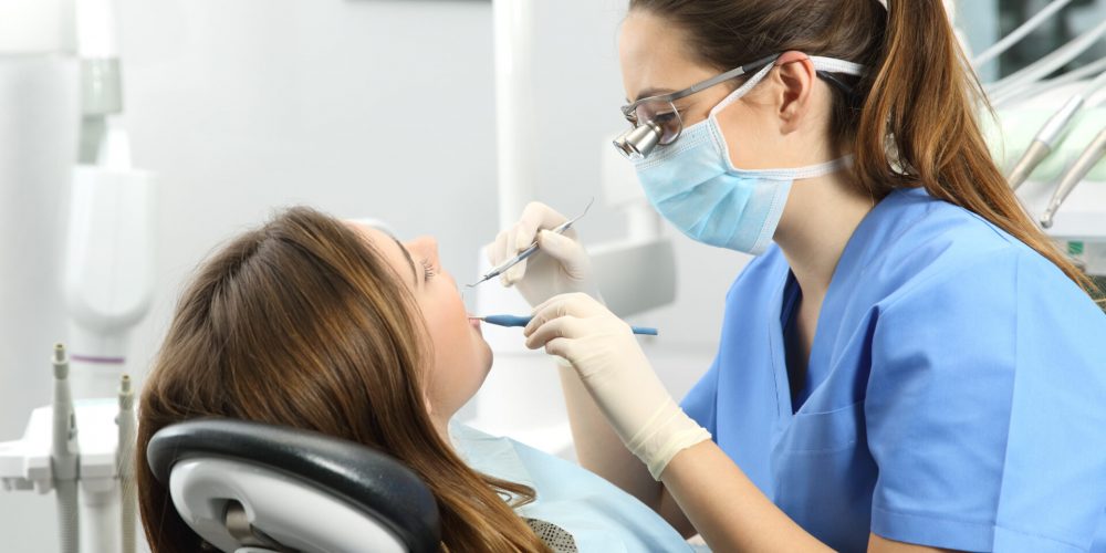 Dentist,Wearing,Eyeglasses,Gloves,And,Mask,Examining,A,Patient,Teeth